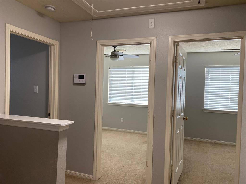 This room features neutral gray walls, a round window providing natural light, a ceiling fan for comfort, and carpeted flooring.