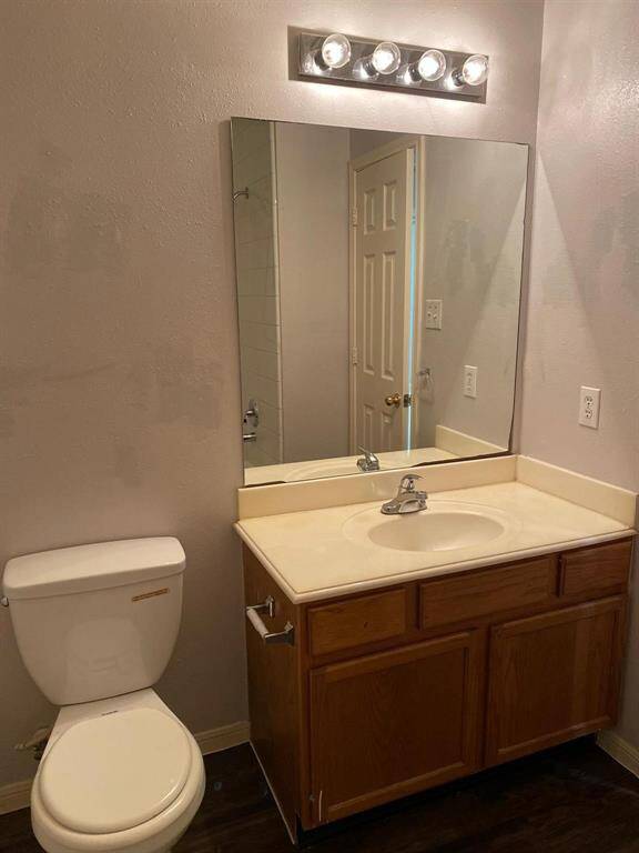 This photo shows a hallway with beige carpet and light gray walls, leading to two rooms with white doors. Both rooms are bright with natural light from windows with blinds. A ceiling fan is visible in one room.