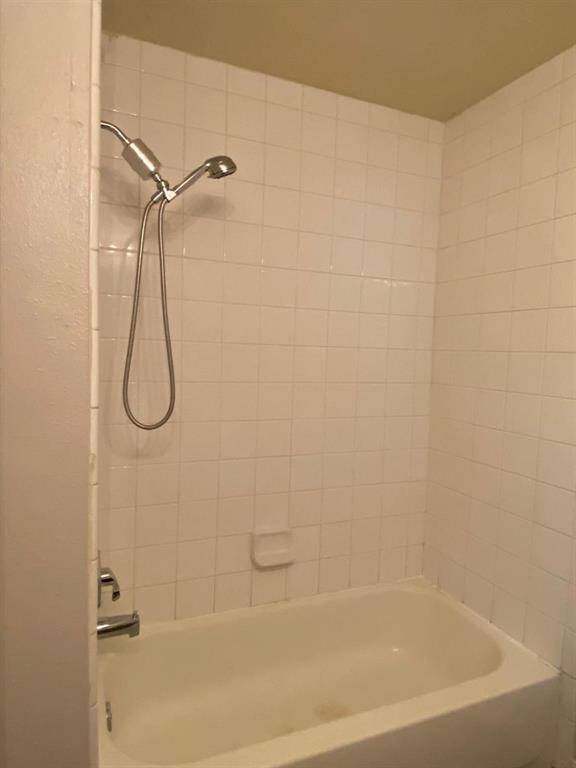 This photo shows a small hallway with light gray walls and carpet flooring. It features a simple ceiling light fixture. There's a bathroom visible on the left with a vanity and mirror, and a doorway leading to another room on the right.