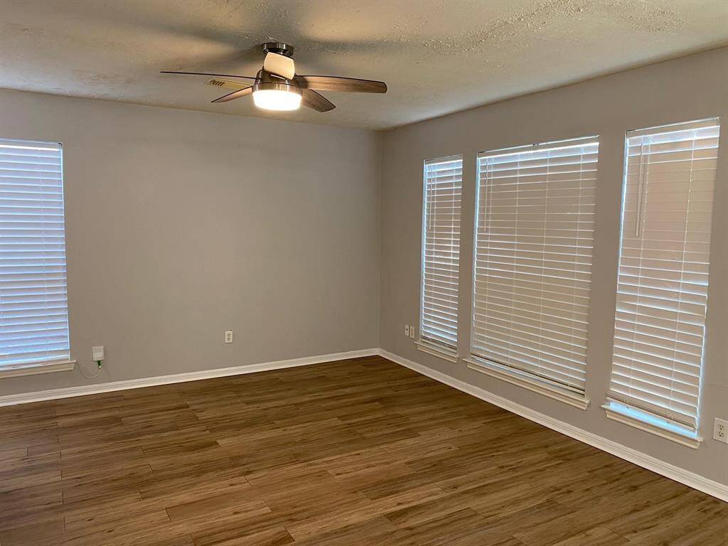 This photo shows a spacious open-plan living area with wood-style flooring. It features a modern kitchen with stainless steel appliances, light gray walls, and ample natural light.