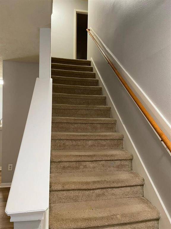 This room features a modern, open layout with wood-like flooring, neutral walls, and ample natural light from large windows. It includes a ceiling fan and a staircase leading to the upper level. Ideal for a cozy living space.
