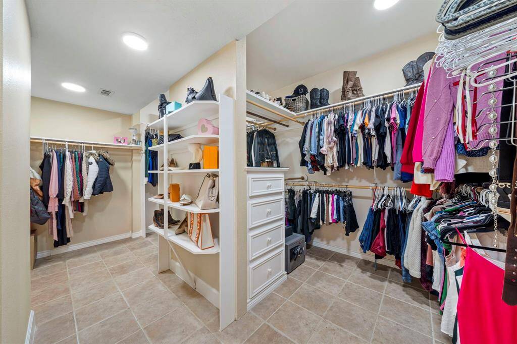 A woman's dream walk-in closet with lots of shelving, drawers on both sides and hanging space. Perfect for organizing clothes, shoes, and accessories. Bright lighting and tiled flooring enhance functionality.
