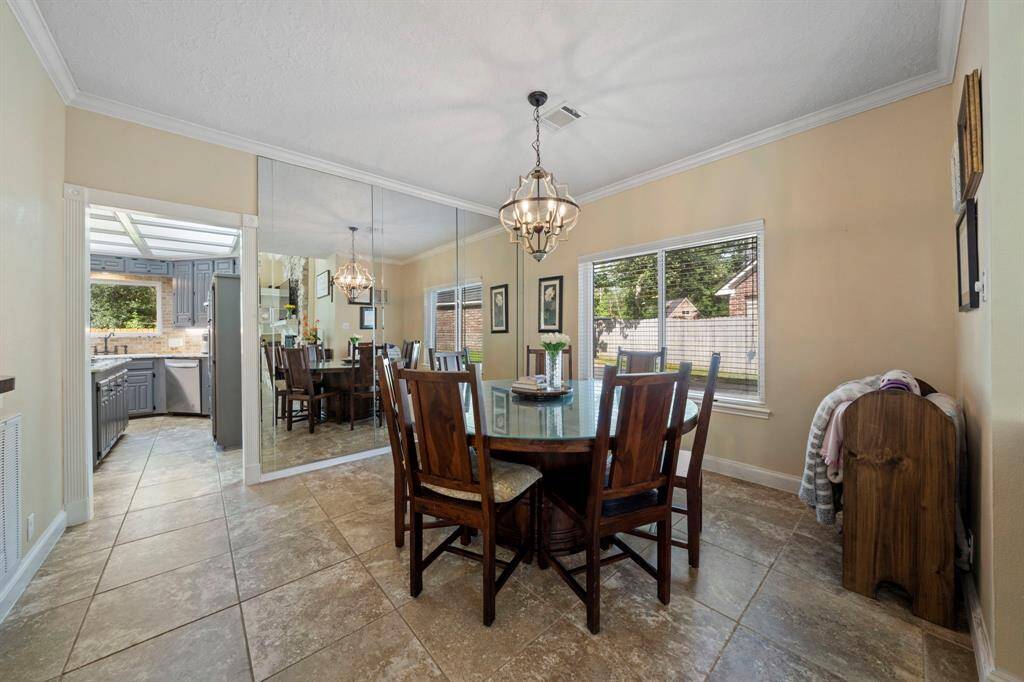 This dining area features a large mirrored backdrop wall with ample natural light from two double paned windows. The space connects to the kitchen with modern cabinetry and tiled flooring, creating a welcoming atmosphere for meals.