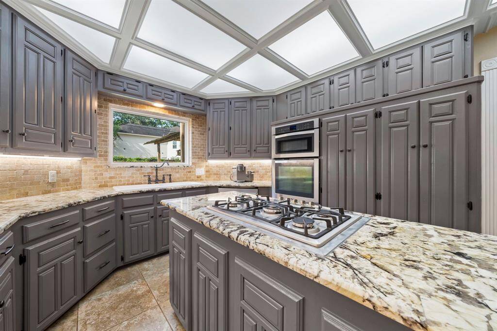 This kitchen offers ample storage, granite countertops, and a modern gas cooktop on the island. The brick backsplash adds a rustic touch, while the large window provides natural light and a pleasant view.