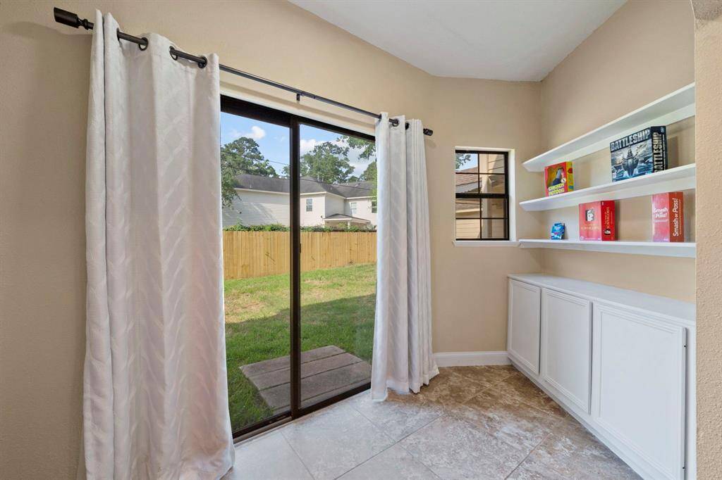 This bright, cozy nook adjacent to the kitchen includes sliding glass doors leading to a fenced backyard. It includes built-in shelves and cabinets, offering plenty of storage. Natural light fills the space, creating a welcoming atmosphere.