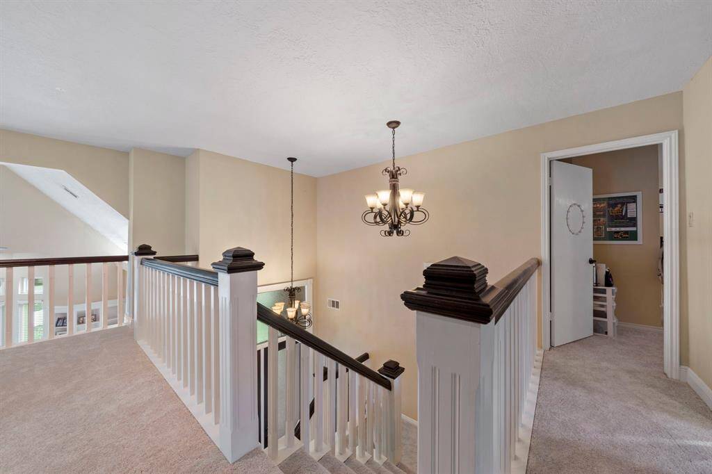Upstairs landing area with new carpet and a stylish chandelier. It features a railing with dark wood accents. The space is well-lit and inviting.