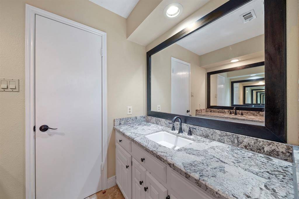 This photo showcases a modern bathroom with two granite countertops side by side featuring a single sink on each counter and lots of vanity space.