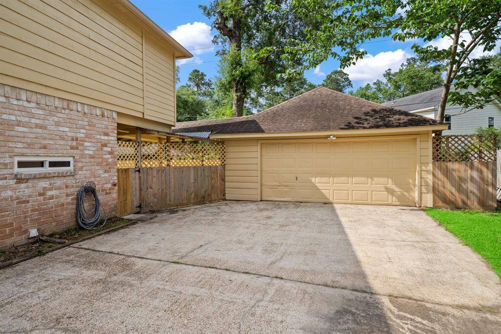 Look at this extra spacious driveway leading to a two-car garage. The area is bordered by a wooden fence and surrounded by greenery, offering privacy and a welcoming outdoor space.