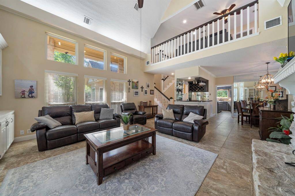 This huge living area features cathedral high ceilings and abundant natural light through large double pane windows. It includes a Stone fireplace, and a view of a loft. The open layout leads to a dining area with elegant lighting, perfect for entertaining.
