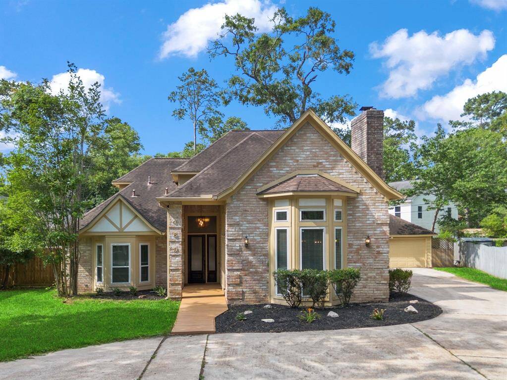 This charming home features a brick exterior with a peaked roof and large bay double pane windows. It has a well-maintained front yard, a circular driveway that leads to a detached 2 car garage, and is surrounded by mature trees, offering a serene and private setting.