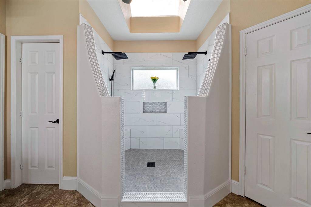 This Primary modern walk-in shower with dual rainfall showerheads, elegant tile work, and a skylight for natural light.