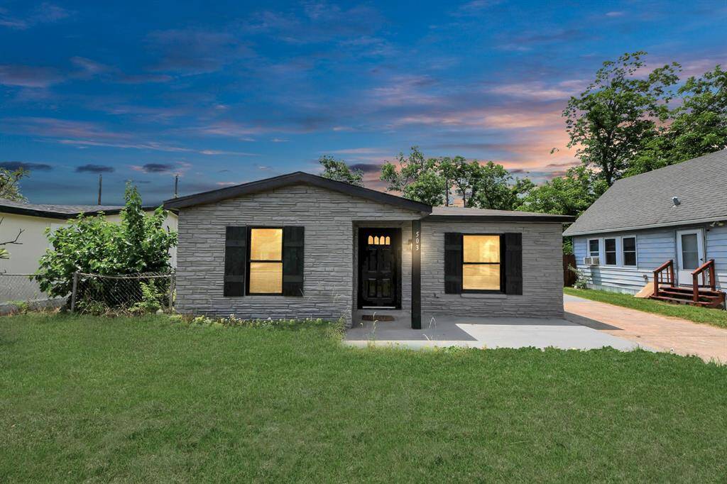 This charming home features a stone facade, black shutters, and a welcoming front porch. It sits on a spacious lawn, ideal for outdoor activities, with a paved driveway leading to the entrance. The sky at dusk adds a serene backdrop.