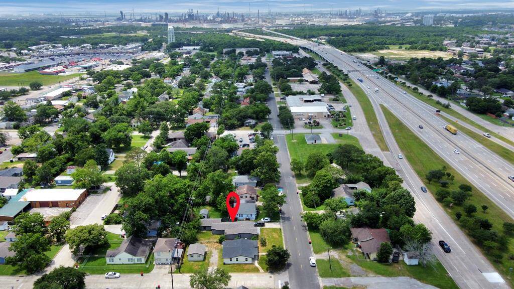 This aerial photo shows a suburban neighborhood with tree-lined streets and a mix of residential homes. A major highway is nearby, providing easy access to the area. The marked location indicates a specific property within this green, well-connected community.