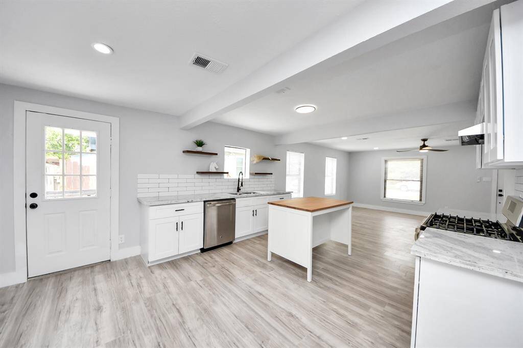 Bright, open-concept kitchen and living area with modern finishes. Features light wood flooring, white cabinetry, stainless steel appliances, and a central island. Abundant natural light complements the clean, contemporary design.