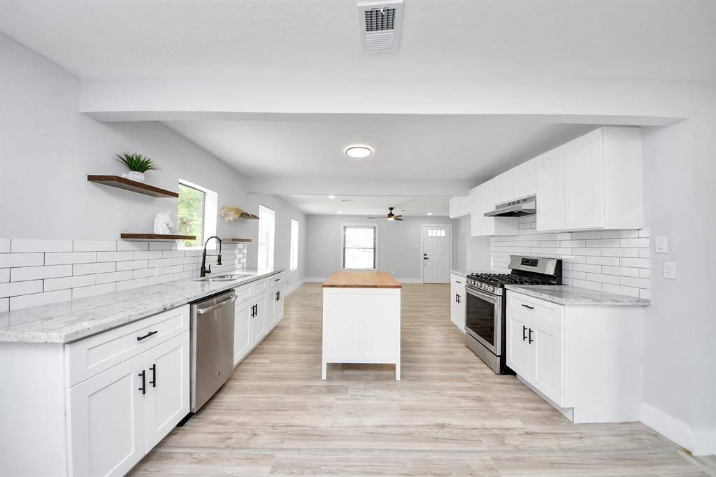 This modern kitchen features sleek white cabinetry, stainless steel appliances, and a spacious island. It has light wood flooring and ample natural light, creating a bright and inviting atmosphere.