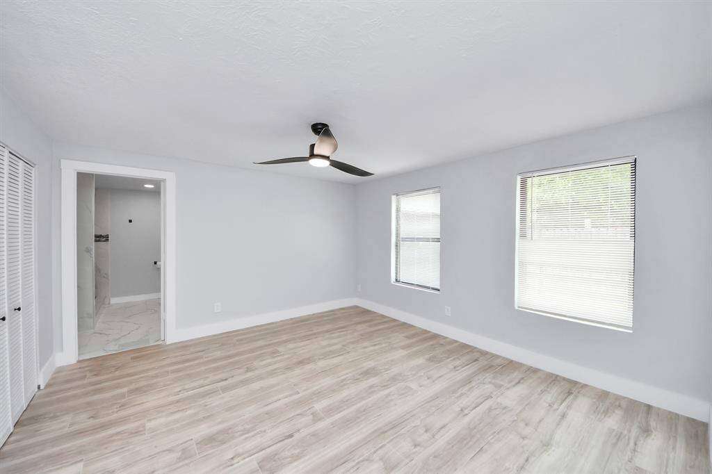 Bright and spacious bedroom with modern laminate flooring, a ceiling fan, and large windows for natural light. Includes an en-suite bathroom with elegant tilework.