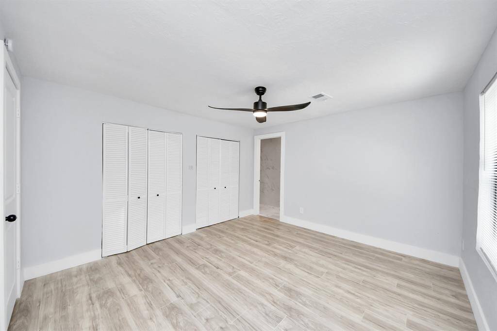 Bright and spacious bedroom with light wood flooring, a modern ceiling fan, and ample natural light. Features double closet doors and neutral walls, offering a clean and inviting space.