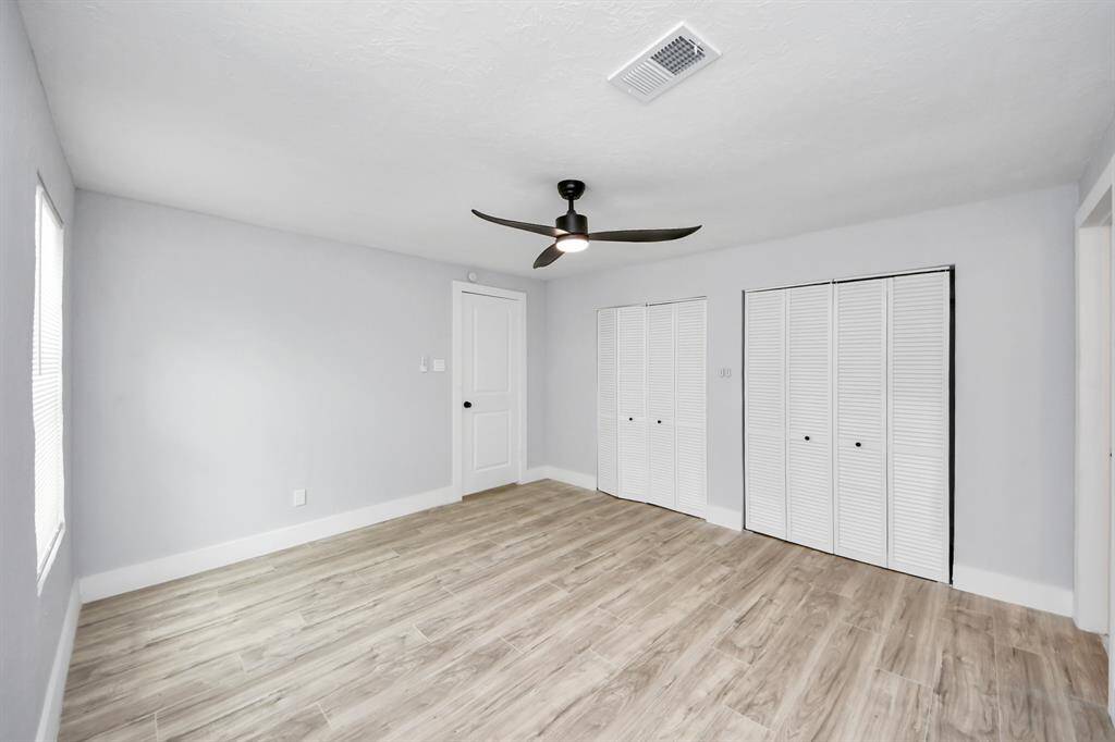 This room features a modern ceiling fan, light wood flooring, and ample natural light. It includes a closet with white louvered doors and has a fresh, neutral color scheme.