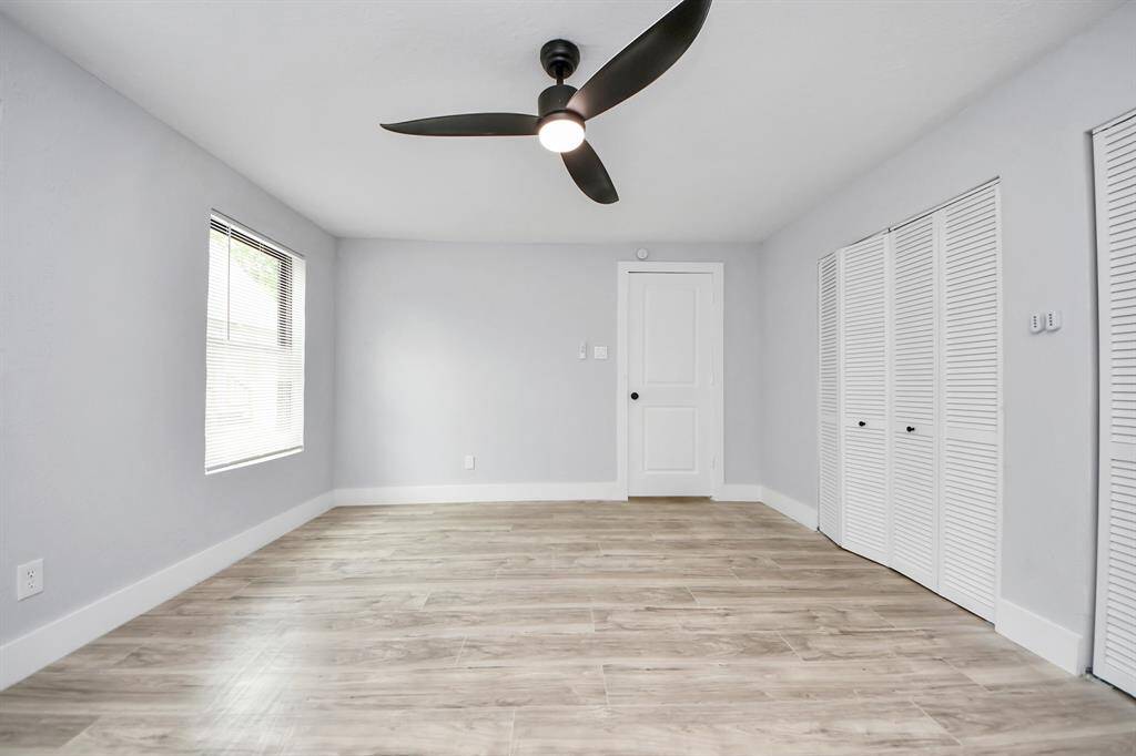 Bright, spacious room with light wood flooring, neutral walls, and a modern ceiling fan. Features a window for natural light and a closet with louvered doors.