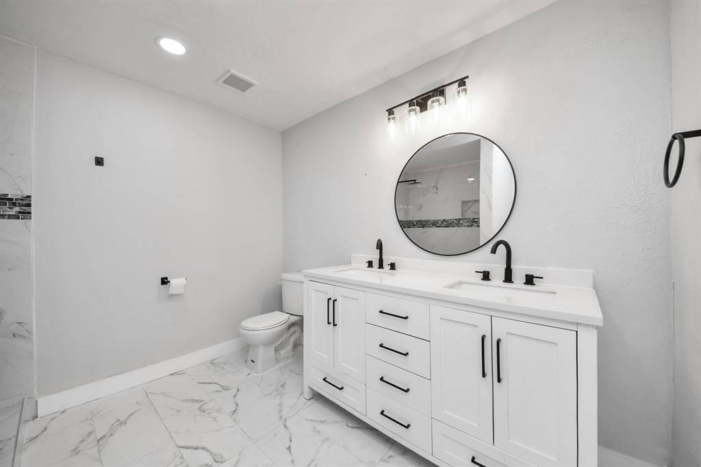 Modern bathroom with sleek design, featuring a double vanity with black fixtures, a round mirror, and marble tile flooring. Bright lighting and neutral tones create a clean, contemporary look.