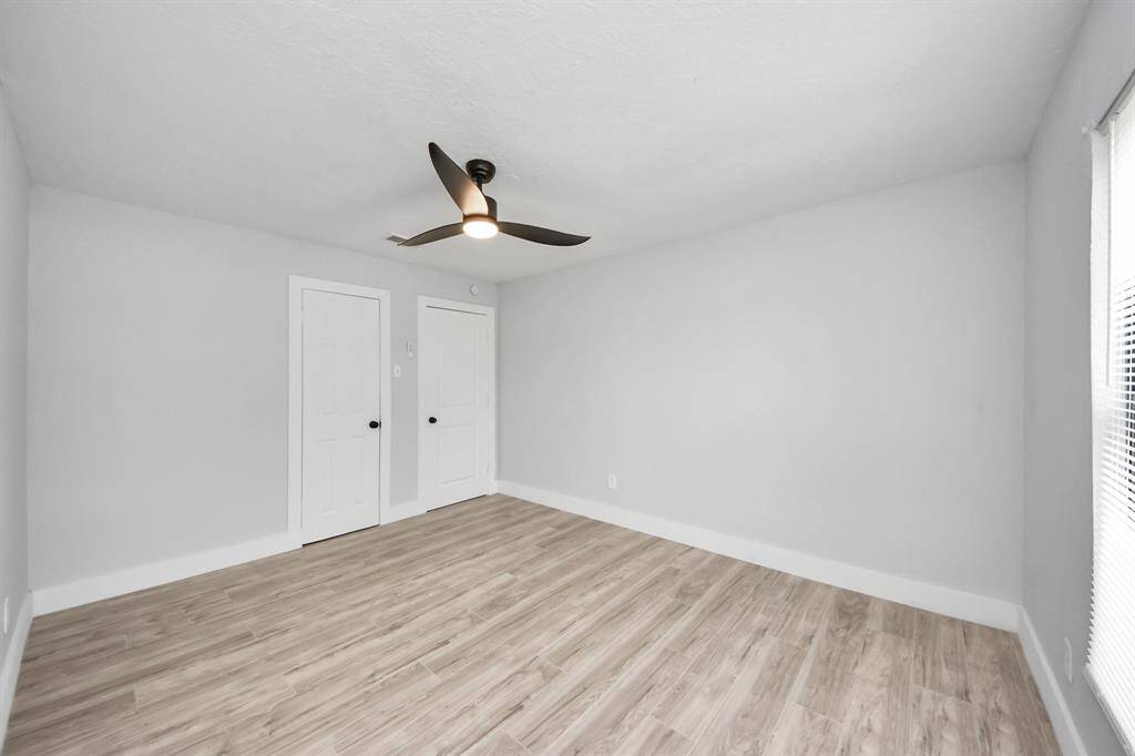 This photo shows a bright, spacious room with light wood flooring, neutral gray walls, a modern ceiling fan, and two white doors, offering a clean and versatile space.