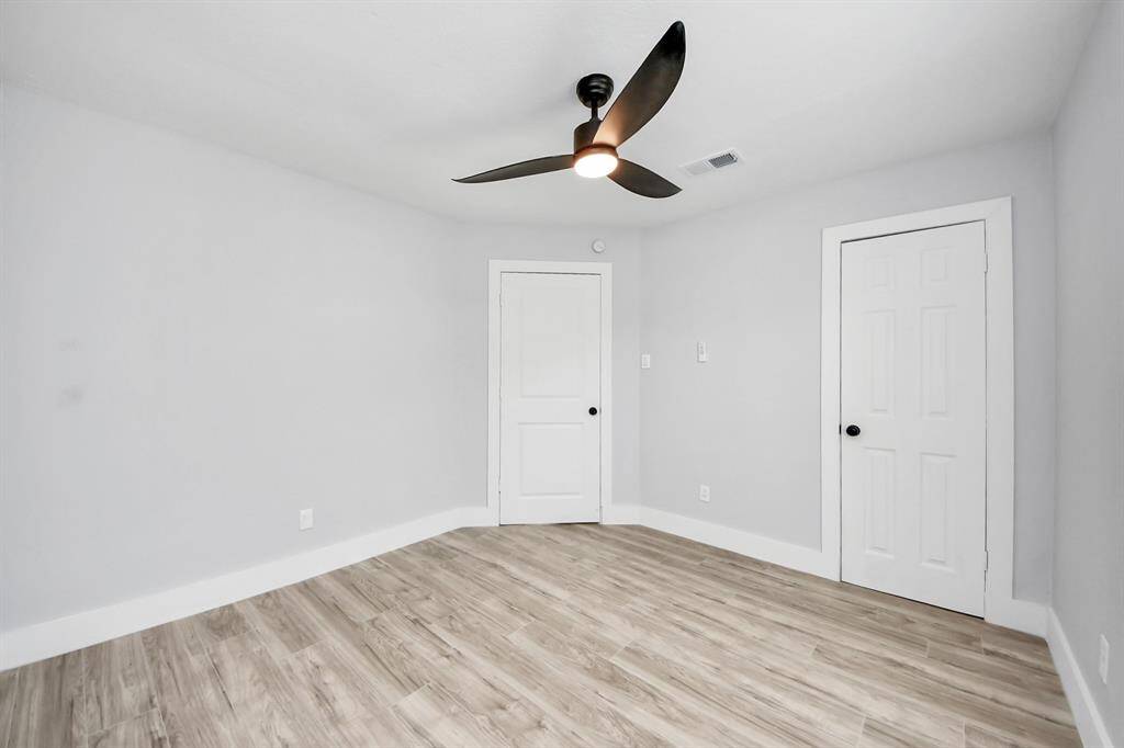 This bright, modern bedroom features light wood flooring and soft gray walls. It includes a sleek ceiling fan and two white doors, offering a clean and contemporary look.