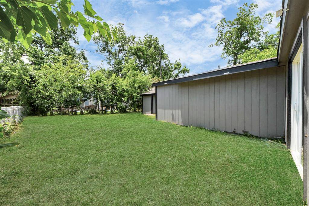 This photo shows a spacious backyard with a well-maintained lawn and surrounding trees providing natural privacy. The exterior of a house with a modern, neutral-toned facade is visible on the right, offering a serene outdoor space perfect for relaxation or entertaining.