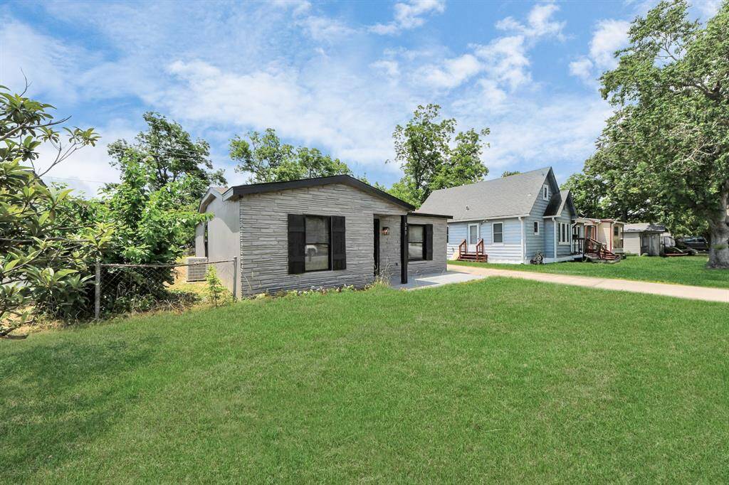 This photo shows a cozy, single-story home with a modern exterior, featuring a stone facade and black shutters. It's surrounded by a well-maintained lawn and mature trees, providing a serene setting. A neighboring house is visible, indicating a friendly, residential neighborhood.