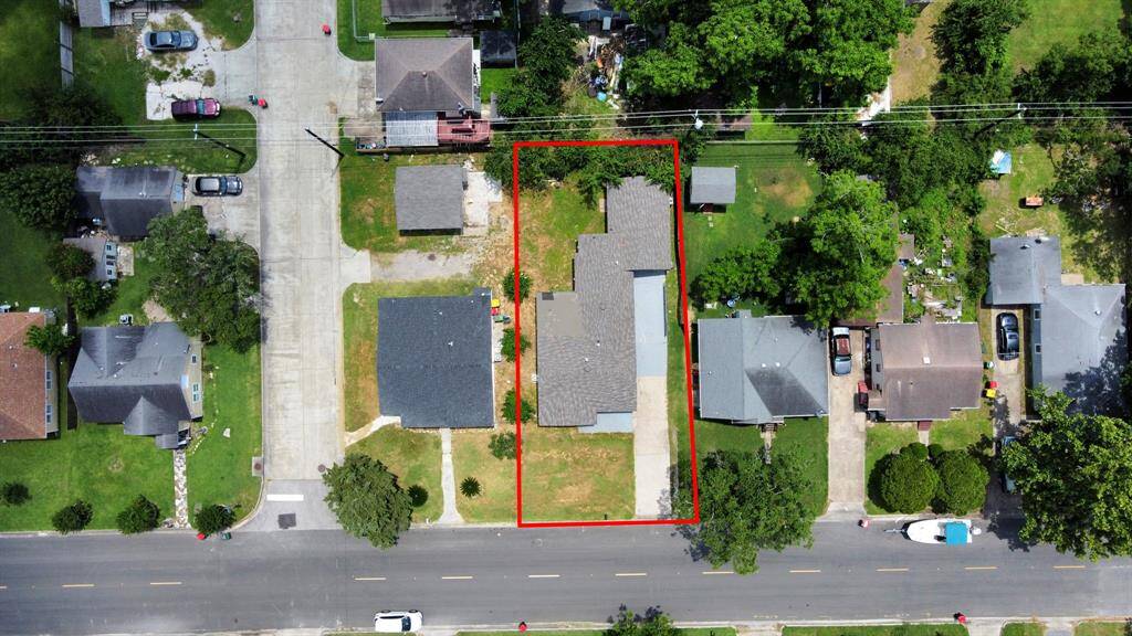 This aerial photo shows a single-story house outlined in red, situated in a suburban neighborhood. The property includes a driveway and a spacious backyard, surrounded by greenery and neighboring homes. The street in front is a quiet residential road.