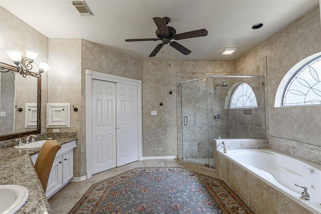 This spacious bathroom features a luxurious bathtub, an oversized tile shower, and dual vanities with plenty of storage, all enhanced by natural light.