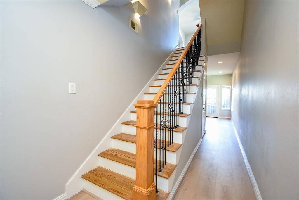 This photo showcases a bright, open living space with hardwood floors and ample natural light from large windows. An arched entryway leads to a dining area, complemented by a stylish chandelier and neutral wall colors, creating a warm and inviting atmosphere.