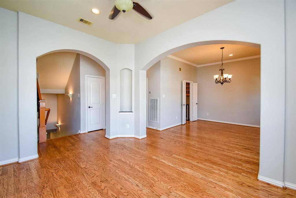 This home features a spacious, open-concept living area with elegant archways and hardwood floors. The room is well-lit and includes a cozy dining space with a chandelier. A staircase to the side leads to an upper level, enhancing the home's charm and functionality.