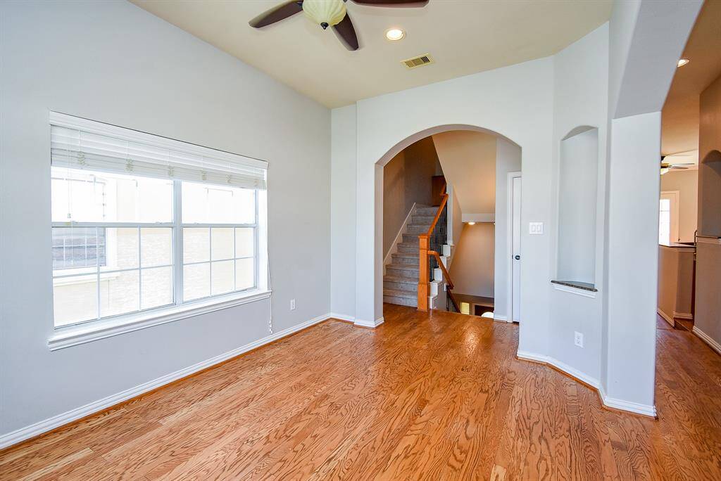 This is a bright dining room featuring hardwood floors, light-color walls, and a ceiling with crown molding. It has a classic chandelier and two large windows providing ample natural light.