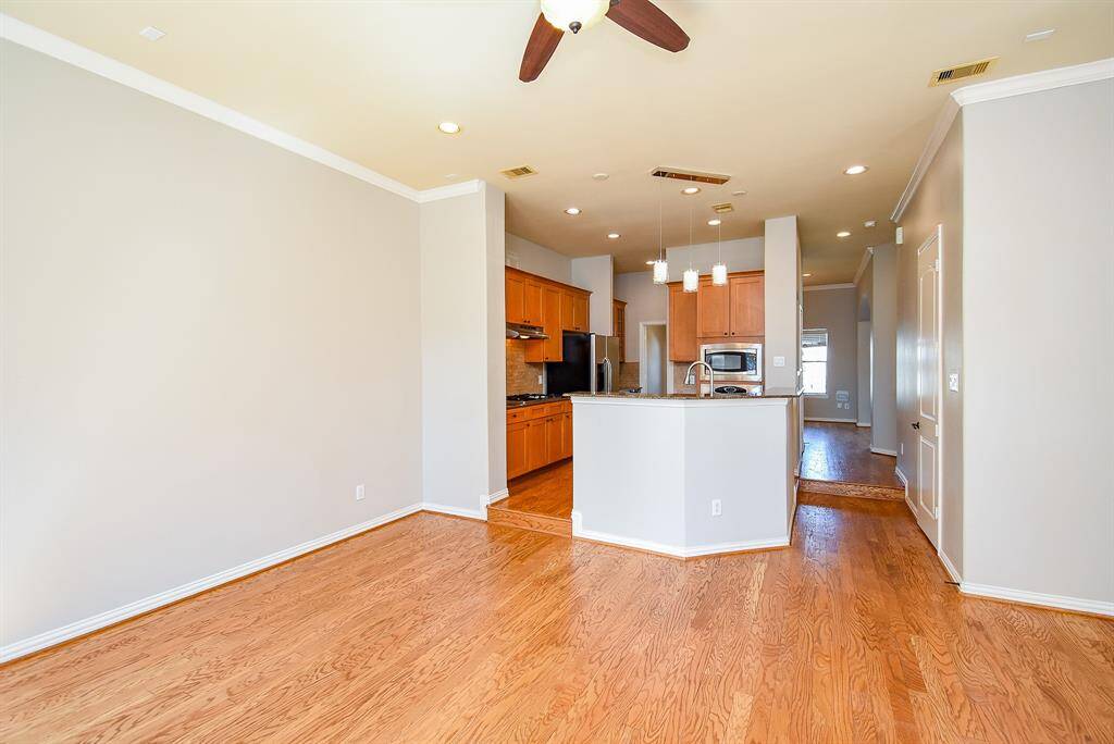 This photo showcases a bright, open-concept kitchen and living area with hardwood floors, neutral walls, and recessed and pendant lighting. The kitchen features warm wood cabinetry.
