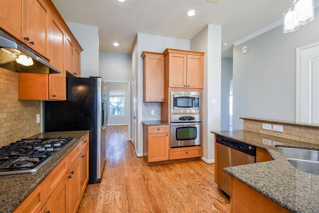 This photo showcases a spacious kitchen with a gas cooktop, tile backsplash, and a breakfast bar.