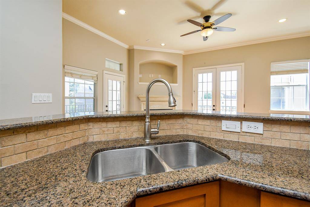 This photo shows a cozy kitchen area with wooden glass cabinets, a granite countertop, and a tiled backsplash.