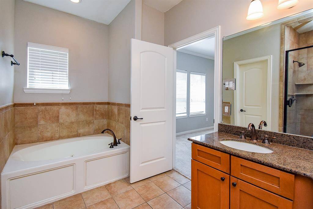 This bathroom features a spacious double vanity with granite countertops and elegant fixtures. It includes a large mirror, a glass-enclosed shower with stylish tile work, and ample lighting. The neutral color palette creates a warm and inviting atmosphere.