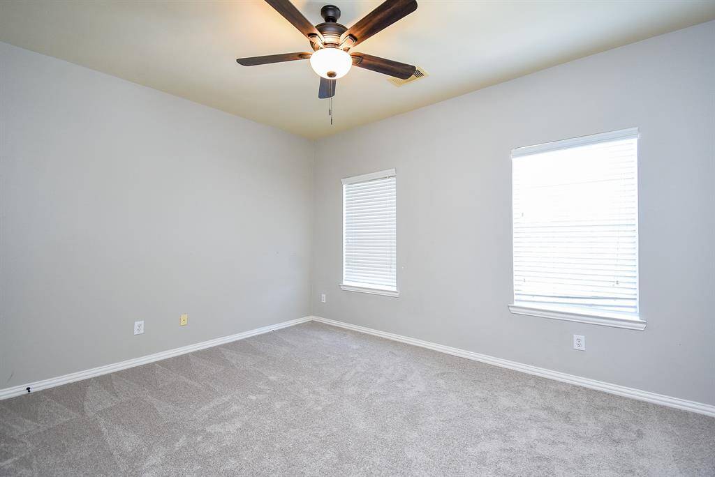 Bright, carpeted room with neutral walls, featuring two windows for natural light and a ceiling fan for comfort.