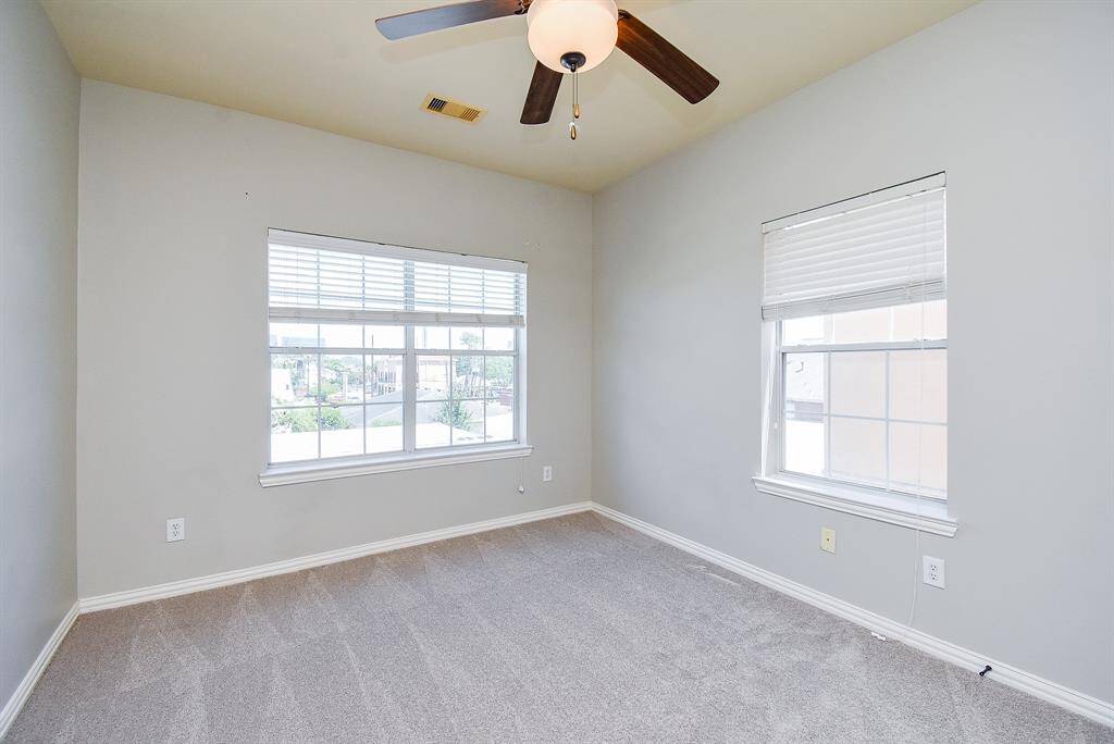 This secondary bathroom features a granite countertop with a single sink, warm wood cabinetry, and a shower-tub combo with tile walls. It has a spacious mirror and modern fixtures, offering a clean and inviting look.