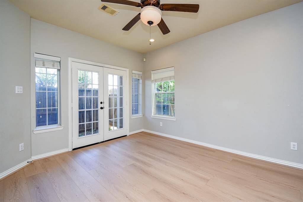 This spacious bedroom on the first floor features a neutral color palette with light wood flooring, a ceiling fan with lighting, and a large window providing natural light.