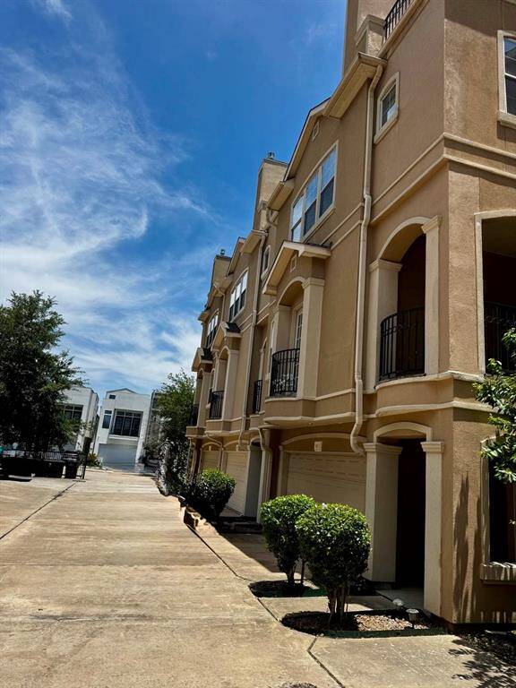 A row of modern townhouses with a stucco exterior and decorative balconies. Each unit features a two-car garage and a neatly maintained driveway. The architecture is contemporary, with clean lines and large windows, offering appealing facade.