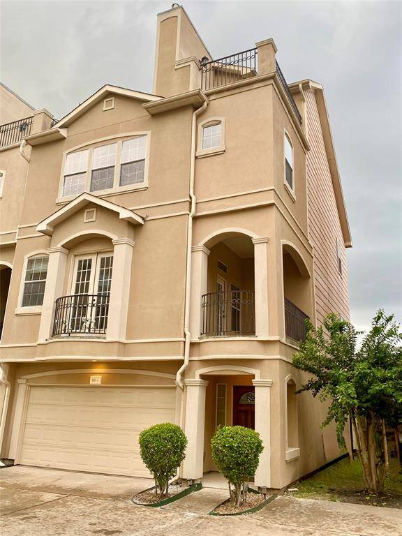 This photo showcases  a welcoming wooden front door. The exterior features a clean, stucco finish with decorative columns and neatly trimmed bushes lining the entrance.