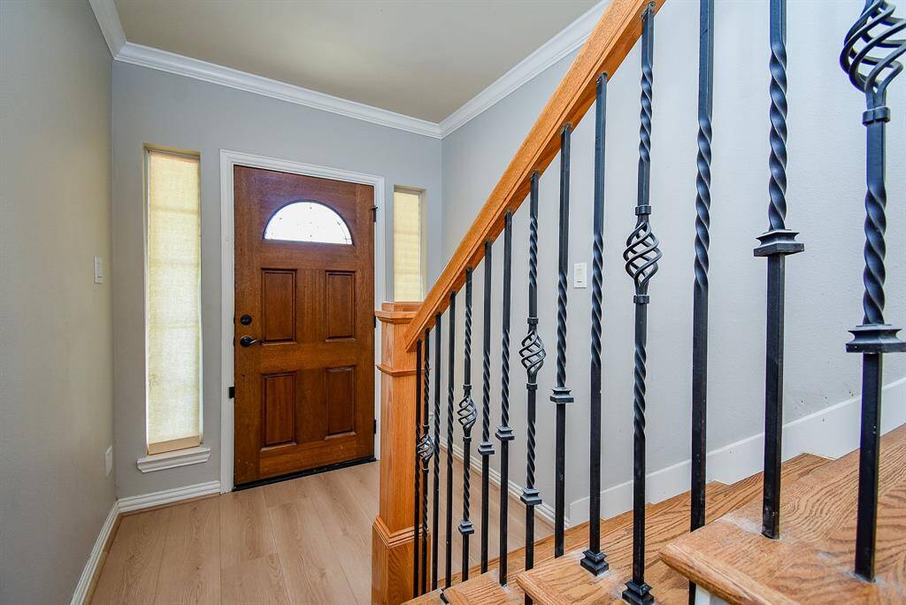 Bright and inviting hallway with light wood flooring, featuring a stylish staircase with wooden steps and decorative wrought iron railings. The space leads to a well-lit area with patio doors, creating an open and airy feel.
