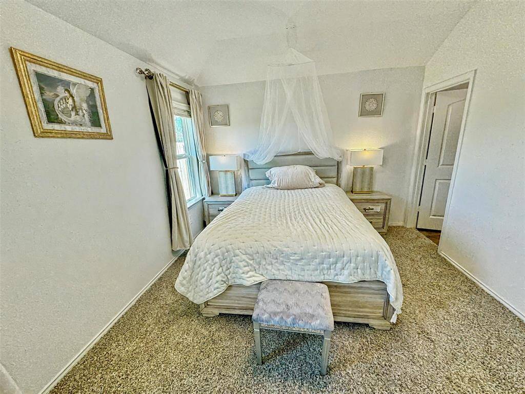 Primary bedroom with a neutral color palette plush carpet, and ample natural light from a window. All bedrooms and living area have remote controlled LED ceiling fan lights.