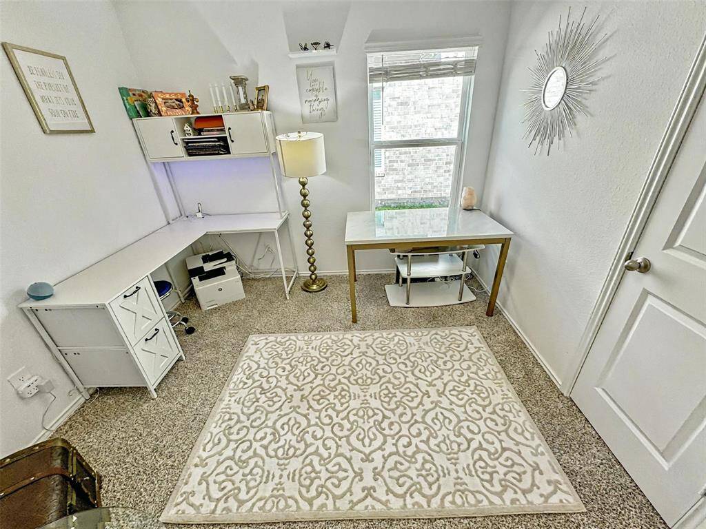 This is a bright, cozy room ideal for a home office or study. It features a soft carpet, a clean white color palette, and ample natural light from the window perfect for work or reading.