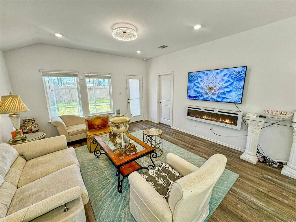 This bright living room features a cozy seating area, and an electric fireplace. Large windows let in plenty of natural light, and the space is accented with tasteful decor and a modern light fixture.