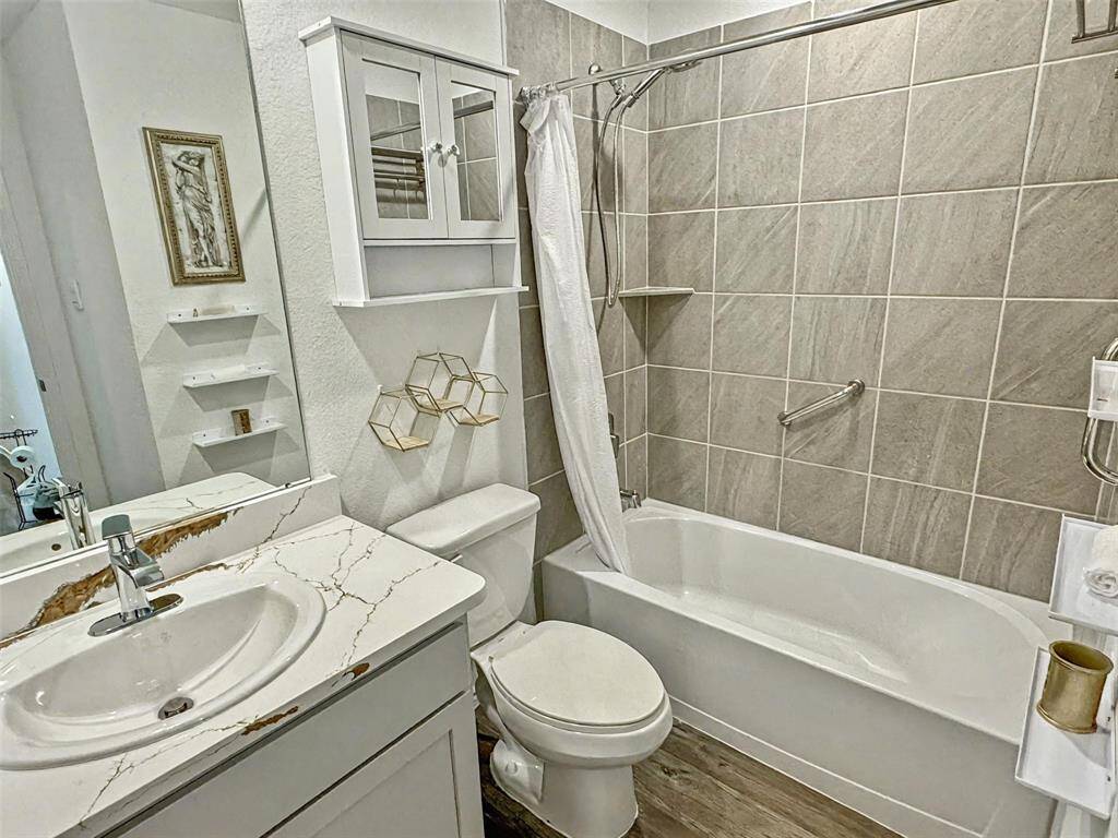Modern bathroom featuring a sleek vanity with  upgraded quartz countertop, a spacious bathtub with tiled walls, and convenient storage solutions including a cabinet and open shelves.