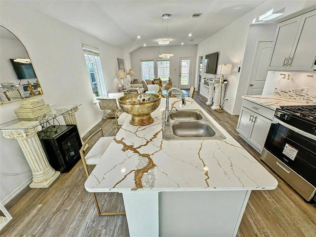Bright and modern kitchen with Calcatta quartz countertops, stainless steel appliances, and ample cabinetry. Features a cozy breakfast bar with seating and elegant LVP wood flooring, creating a welcoming atmosphere.