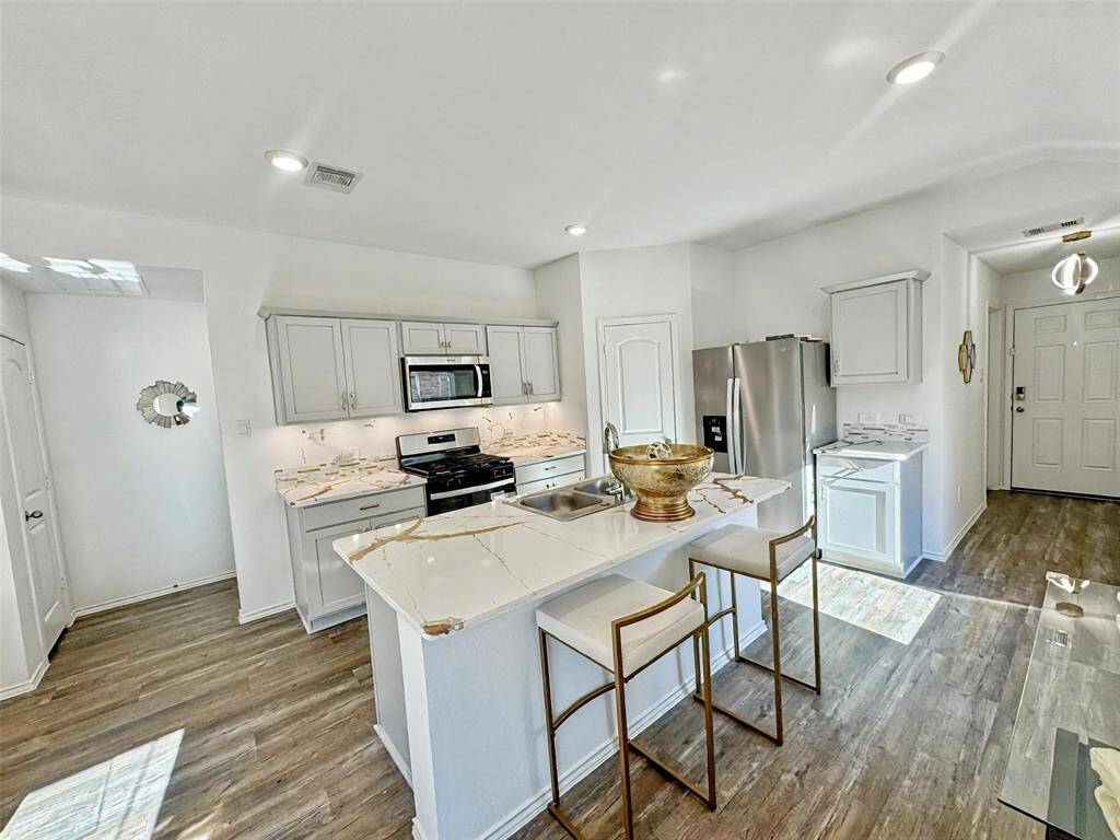 Bright and modern kitchen with Calcatta countertops, stainless steel appliances, and ample cabinetry. Features a cozy breakfast bar with seating and elegant LVP wood flooring, creating a welcoming atmosphere.