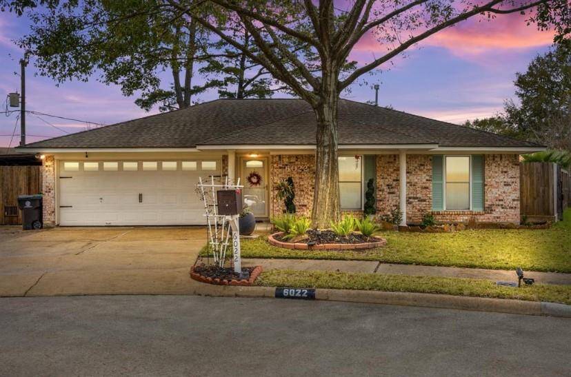 Charming single-story brick home with a two-car garage, nestled on a quiet cul-de-sac. The well-maintained front yard features mature trees and inviting landscaping, beautifully lit by the warm evening glow.